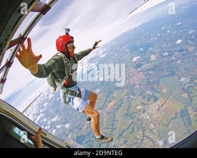 Paracadutista coraggioso con casco rosso saltare fuori dall'aereo Foto Stock