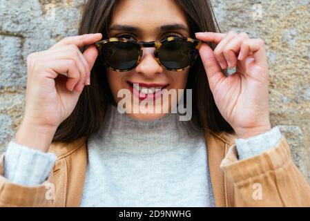 Bella giovane donna che posa su una parete con occhiali da sole Foto Stock