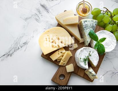Vari tipi di formaggio, uva e miele su sfondo marmoreo Foto Stock