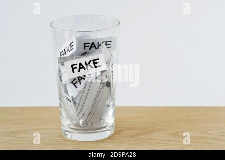 Vetro dell'acqua con i pezzi di carta con le notizie ed il Word Fake - concetto di notizie false Foto Stock