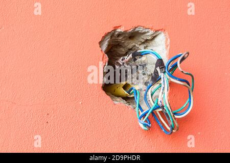 rompere la parete del foro con fili elettrici colorati, copyspace sulla sinistra. Foto Stock