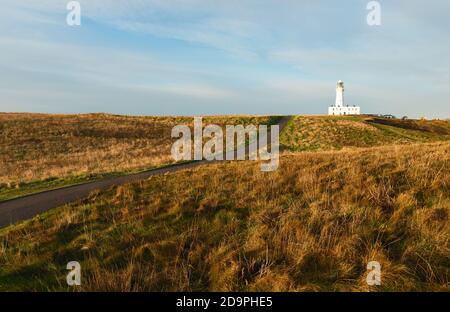 Faro sotto il cielo blu con erba e strada che corre in mezzo in primo piano all'alba in autunno a Flamborough, Yorkshire, Regno Unito. Foto Stock