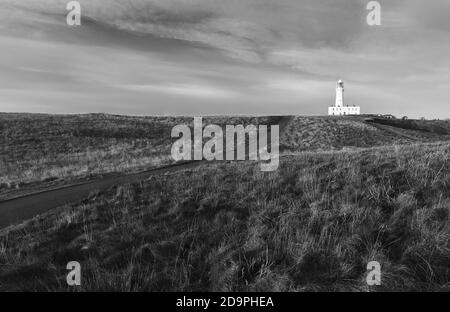 Faro sotto il cielo blu con erba e strada che corre in mezzo in primo piano all'alba in autunno a Flamborough, Yorkshire, Regno Unito. Foto Stock