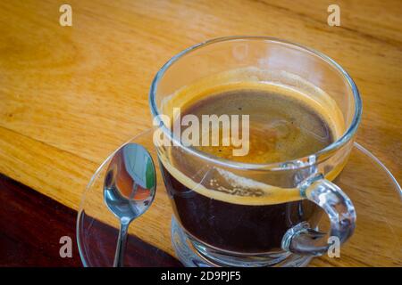 Caffè espresso nero in piccola tazza di vetro su tavolo di legno con cucchiaino da tè Foto Stock
