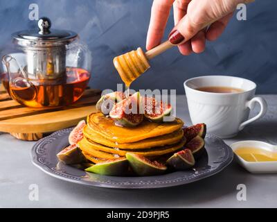 Pila di frittelle di zucca con fichi e miele e tè caldo. Cibo di autunno sfondo blu su sfondo grigio Foto Stock