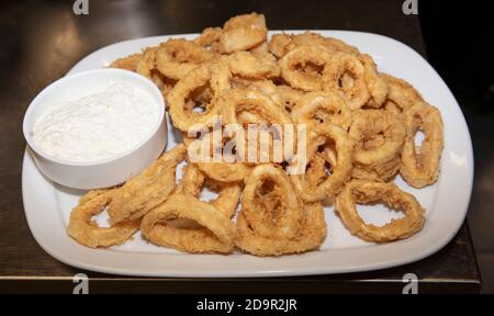 Anelli di calamari fritti con condimento di insalata su piatto bianco in un ristorante. Anelli di Calamari fritti profondi in olio bollente. Foto Stock