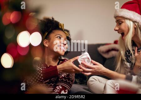 Due fidanzate scambiano insieme i regali di Natale; concetto di celebrazione di natale domestico Foto Stock