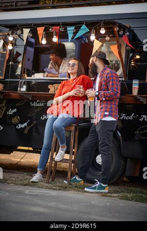 giovane coppia caucasica urbana che flirta davanti al camion modificato per il servizio di fast food mobile Foto Stock
