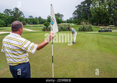 Louisiana Northshore, Mandeville, Beau Chene Country Club campo da golf golfisti giocare a putting verde, uomo uomini amici tenendo bandiera, Foto Stock