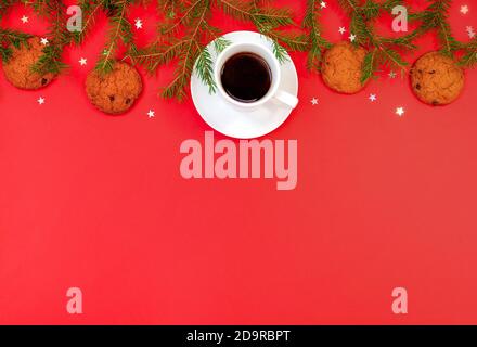 Sfondo natalizio con rami di abete, una tazza di caffè e biscotti al cioccolato con fiocchi d'avena su uno sfondo rosso brillante Foto Stock