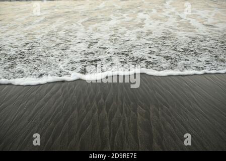 Closeup di schiumosa onda oceanica che raggiunge la riva. Bella struttura ondulata / modello su sabbia nera. Santa Catalina, Panama, America Centrale Foto Stock