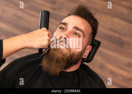 Vista dall'alto di un cliente in un barbiere, la sua barba viene tagliata e tagliata con un rasoio elettrico Foto Stock