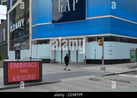 Un uomo che indossa una maschera cammina di fronte a un chiuso e si è imbarcato su Gap store in Times Square. Foto Stock