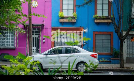 Auto bianca parcheggiata fuori da due case colorate dal quartiere Di Coyoacan Foto Stock