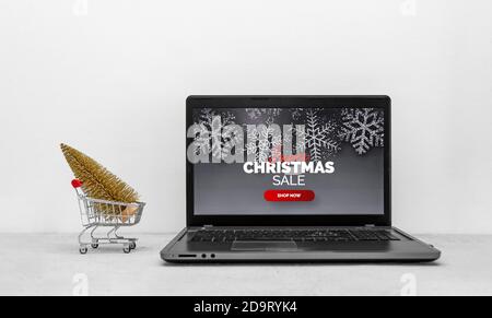 Schermo del portatile che mostra la vendita di Natale, accanto ad un mini carrello della spesa e un piccolo albero d'oro Foto Stock