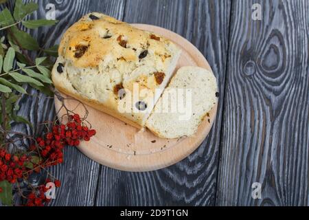 Focaccia con olive e pomodori secchi. Nelle vicinanze si trova un ramo di rowan secco con bacche rosse. Su tavole di pino. Foto Stock