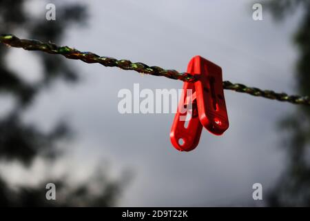 gli abiti isolati in plastica di colore rosso si agganciano su una corda Foto Stock