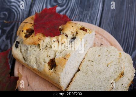 Focaccia con olive e pomodori secchi. Nelle vicinanze si trovano foglie d'autunno secche. Su tavole di pino. Foto Stock