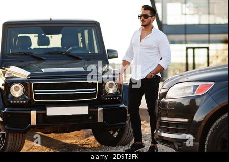 Uomo asiatico solido in camicia bianca e occhiali da sole posati vicino mafia nero suv auto. Foto Stock