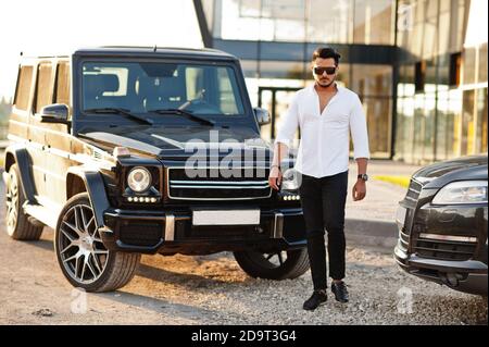 Uomo asiatico solido in camicia bianca e occhiali da sole posati vicino mafia nero suv auto. Foto Stock