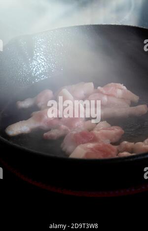 I lardi di pancetta tritati cucinando su un piano cottura in un getto teglia per friggere Foto Stock