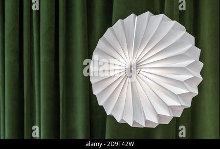 Lampada ondulata rotonda su uno sfondo di tende verdi. Foto Stock