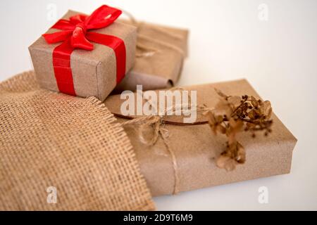 Scatole regalo avvolte in carta artigianale con nastro rosso e. corda rustica naturale su sfondo bianco con fiori di idrangea essiccati Foto Stock