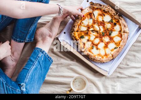 Ragazza seduta sul pavimento su una coperta con una tazza di caffè e una pizza, vista dall'alto Foto Stock