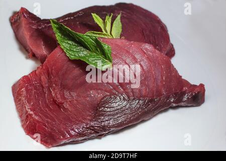 Due fette di tonno rosso fresco crudo su un piatto con menta Foto Stock