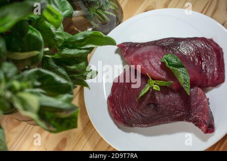 Due fette di tonno rosso fresco crudo su un piatto con menta e basilico Foto Stock
