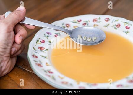 una mano con un cucchiaio di zuppa di alfabeto in un piatto decorato su un tavolo di legno. Sul cucchiaio viene visualizzato il messaggio zuppa Foto Stock