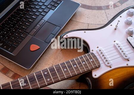 chitarra elettrica accanto a un portatile con un pick online lezioni di chitarra Foto Stock