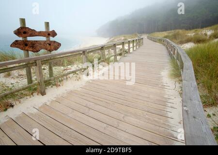 passerella sulla spiaggia in una giornata foggosa con un cartello in legno Foto Stock