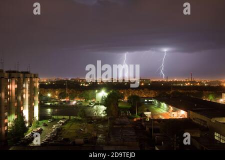 La potente tecnologia thunderbolt colpisce la città di notte. Un forte colpo di fulmine su un cielo grigio scuro colpisce il terreno, illuminando l'area industriale circostante Foto Stock