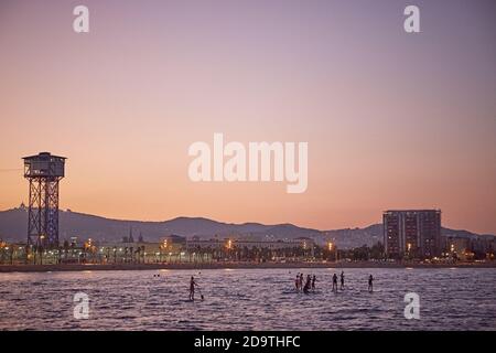 Barcellona, Spagna, settembre 2019. Persone che giocano a paddle surf al tramonto a Barceloneta con la città sullo sfondo. Foto Stock