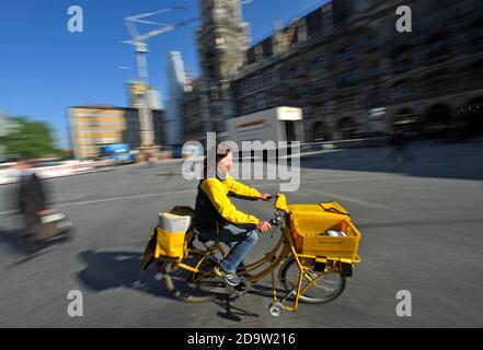 Un addetto postale ptedesco guida una bicicletta di consegna Deutsche Post passando il municipio di Monaco a Marienplatz, nel centro di Monaco. Foto Stock