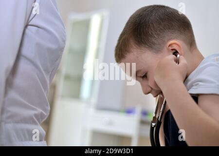 Il ragazzo inserì cuffie stetoscopiche nelle orecchie. Il medico ha un frammento di abbigliamento bianco. Foto Stock