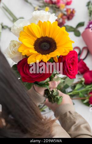 persona che fa con le sue mani un fiore bouquett con girasole, rose nello spazio di lavoro di sfondo Foto Stock