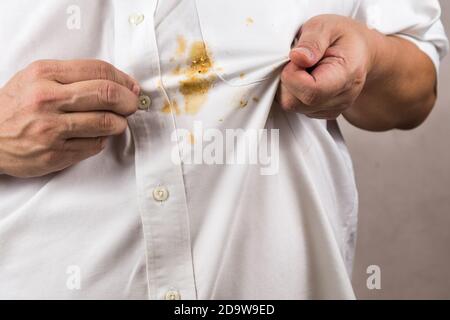 Persona che indica la macchia di curry rovesciata sulla camicia bianca. Foto Stock