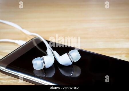 Cuffie o auricolari e smartphone su sfondo in legno. Foto Stock