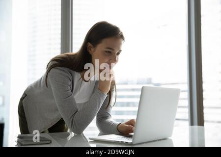 Operatrice interessata che si trova vicino alla scrivania e guarda sullo schermo del computer portatile Foto Stock