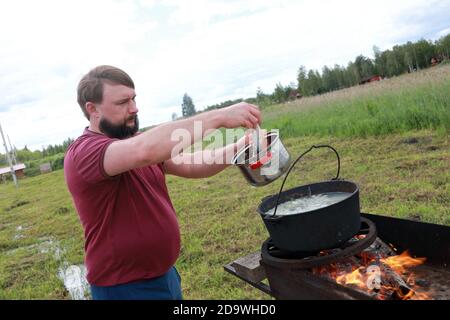 L'uomo mette il pesce di salmone nel calderone per cucinare il pesce russo zuppa - ukha Foto Stock