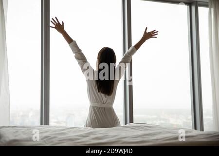 Donna felice seduta nella camera da letto di lusso si è rivolta alla parete della finestra Foto Stock