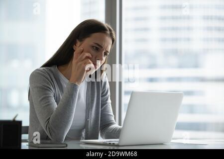 La donna accigliata che guarda lo schermo non riesce a trovare la decisione Foto Stock