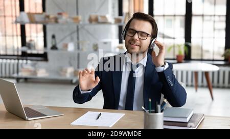 Uomo d'affari rilassato e giovane sorridente che ascolta la musica preferita negli auricolari. Foto Stock