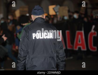 Cracovia / Polonia - 7 novembre 2020: Manifestazione anti-governo a Cracovia, organizzata da Women Strike, poliziotto si trova di fronte alla folla di manifestanti Foto Stock