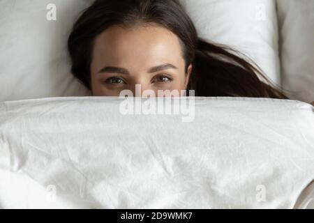 Gioiosa giovane femmina riposante nel letto coprendo il viso con coperta Foto Stock