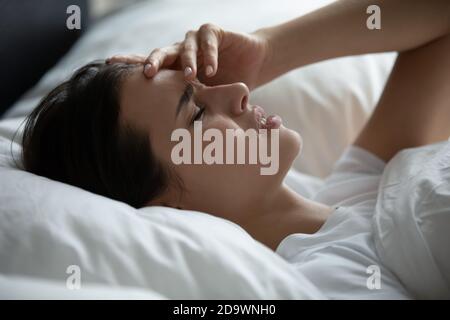 Triste donna sdraiata in cuscini che toccano la fronte affetta da emicrania Foto Stock