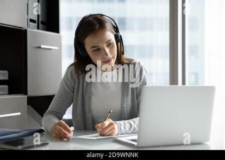 Donna interessata che guarda il webinar in cuffia che scrive le informazioni Foto Stock