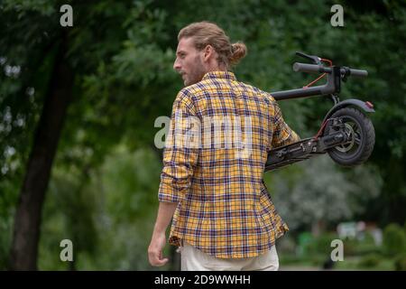 Mattina a piedi. Uomo in camicia a scacchi con lo scooter e guardando da parte Foto Stock